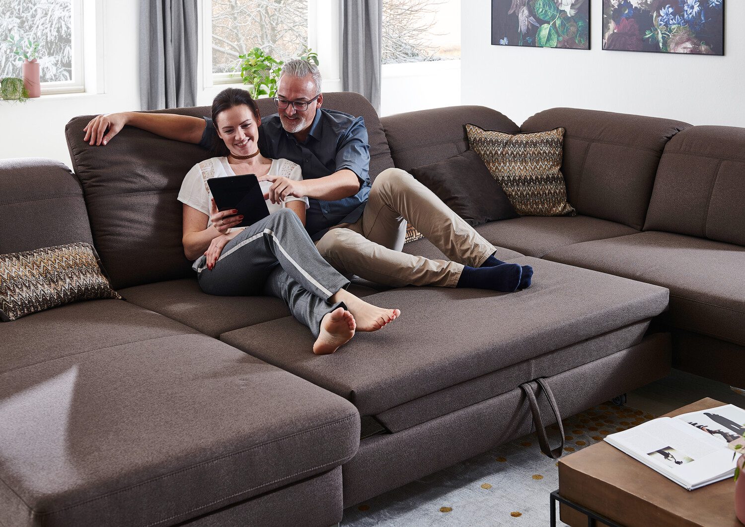 Möbel Abverkauf - Paar sitzt auf gemütlicher Couch und stöbert ine inem Tablet.